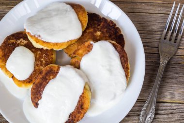 Süzme peynir ile Pancakes, ekşi krema beyaz bir tabak içinde.