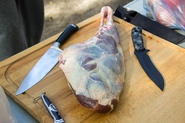 Carne fresca e crua. Perna de cordeiro com facas na tábua de corte — Fotografia de Stock