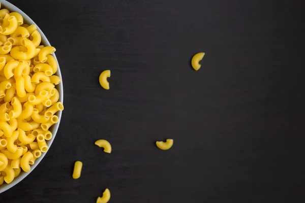 Vista superior de fondo negro con cuernos de pasta cruda italiana en tazón con espacio para copiar — Foto de Stock