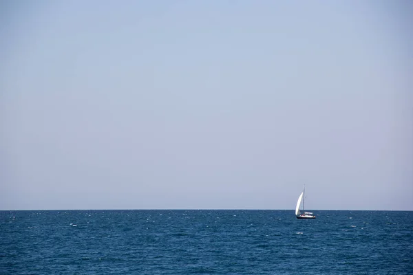 Pequeño yate de vela con grandes velas blancas en mar abierto en el horizonte — Foto de Stock