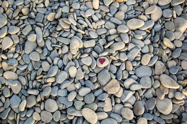 Corazón de piedra pintado con un marcador de pintura roja en el guijarro como regalo para San Valentín en el fondo de guijarro . — Foto de Stock