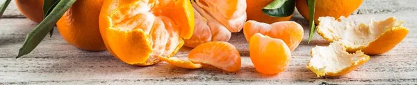 Banner orangefarbener Mandarinen mit grünen Blättern auf weißem Holzgrund. geschälte Mandarinenscheiben — Stockfoto