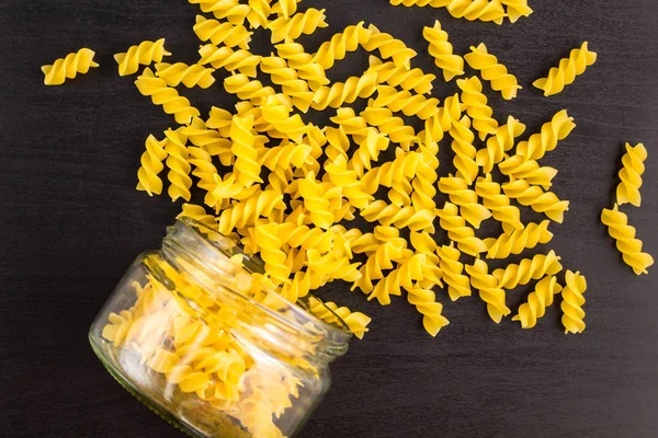 Glasburk fylld med torr pasta spiral Fusilli och spridda runt på svart bakgrund — Stockfoto