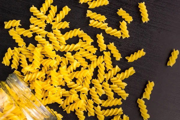 Glasgefäß mit Spiralfusilli gefüllt und auf schwarzem Hintergrund verstreut — Stockfoto