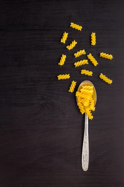 Pasta cruda italiana en espiral fusilli seca sobre una cuchara metálica y una mesa negra — Foto de Stock