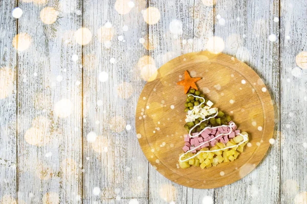 Beyaz ahşap bir masada kesme tahtasındaki salata olivierinden Noel ağacı. Kopyalama alanı olan üst görünüm.