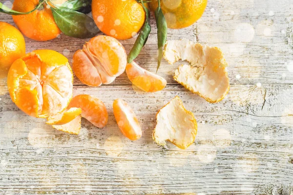 Oranžové mandarinky se zelenými listy na bílém dřevěném pozadí. Loupané mandarínské plátky — Stock fotografie