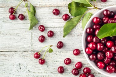 Taze kirazlar, beyaz kase ve ahşap zeminde su damlaları.