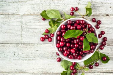 Taze kirazlar, beyaz kase ve ahşap zeminde su damlaları.