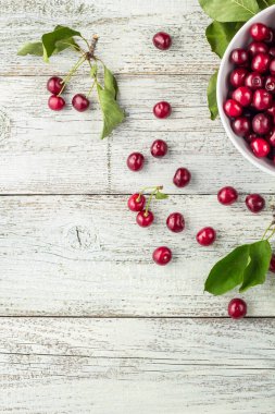 Taze kirazlar, beyaz kase ve ahşap zeminde su damlaları.