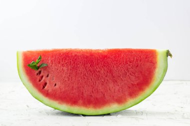 Beyaz arka planda yeşil nane yapraklı taze kırmızı olgun karpuz dilimlenmiş.