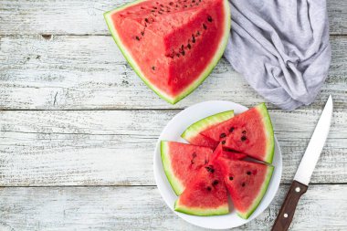Tabakta olgun karpuz dilimleri beyaz ahşap arka planda bir bıçakla peçeteyle