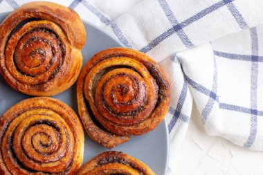 Hafif arka planda gri tabakta tarçınlı çörekler ve kareli peçete. Üst görünüm