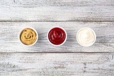 Beyaz ahşap arka planda üç çeşit klasik sos. Mayonez ketçap hardalı. Kopyalama alanı olan üst görünüm