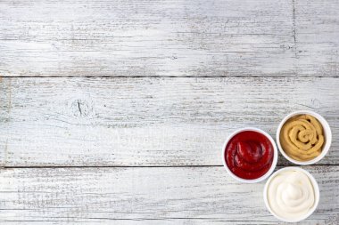 Beyaz ahşap arka planda üç çeşit klasik sos. Mayonez ketçap hardalı. Kopyalama alanı olan üst görünüm
