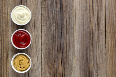 Doğal ahşap arka planda üç çeşit klasik sos. Mayonez ketçap hardalı. Kopyalama alanı olan üst görünüm