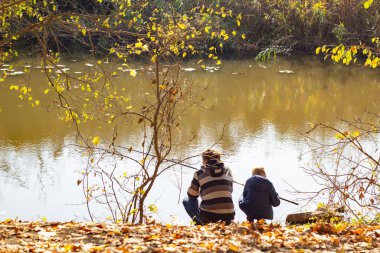 Sonbaharda nehir kenarında balık tutan bir baba ve oğulun arka görüntüsü..