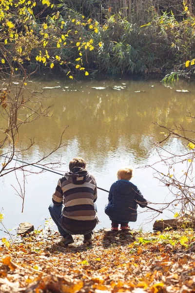 Sonbaharda nehir kenarında balık tutan bir baba ve oğulun arka görüntüsü..