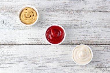 Beyaz ahşap arka planda üç çeşit klasik sos. Mayonez ketçap hardalı. Kopyalama alanı olan üst görünüm