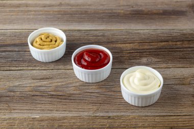 Doğal ahşap arka planda üç çeşit klasik sos. Mayonez ketçap hardalı. Kopyalama alanı olan üst görünüm