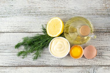 Beyaz ahşap arka planda limon, yumurta, yağ ve bitkilerle mayonez sosu.