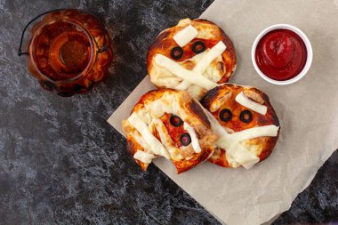 Peynirli, zeytinli ve ketçaplı çocuklar için mumya olarak mini pizza. Karanlık arka plandaki çocuklar için komik çılgın Cadılar Bayramı yemekleri