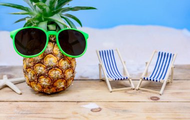 Ahşap arka planda güneş gözlüklü ananas. Minyatür oyuncaklarla yaz tatili konsepti.