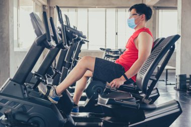 Sporcu adam spor salonunda çalışırken yüz maskesi takar. Sosyal uzaklık ve refah. Sağlıklı ve sağlıklı. Zihin-vücut gelişimi. Yeni normal ve COVID-19 'dan sonraki yaşam.