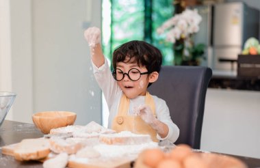 Oğlum yemek pişiriyor. Un ve ekmekle bir malzeme hazırlıyorum. Evdeki günlük çocuk yaşam tarzı. Asyalı aile mutfakta..