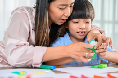 Asyalı anne oğluyla birlikte evde çalışıyor. Anne ve çocuk hamur oynuyorlar. Çocuk plasticine kil modeli yaratıyor. Kadın yaşam tarzı ve aile aktiviteleri.