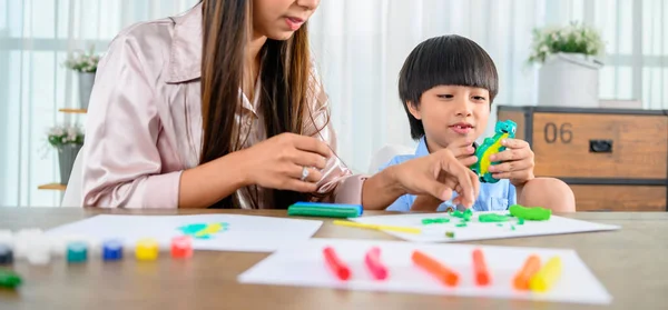 Asian mother work home together with son. Mom and kid play dough. Child creating plasticine clay model. Woman lifestyle and family activity.