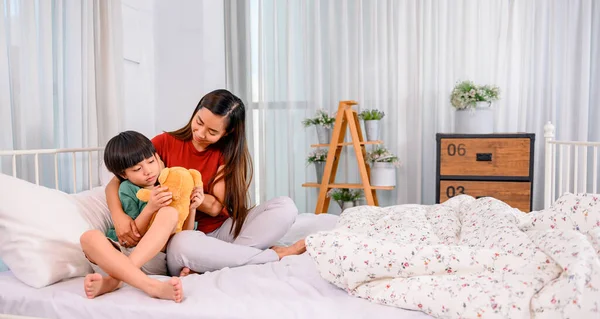 Mom hug and kiss son on the bed. Woman lifestyle and family activity. Asian mother work home together with kid.