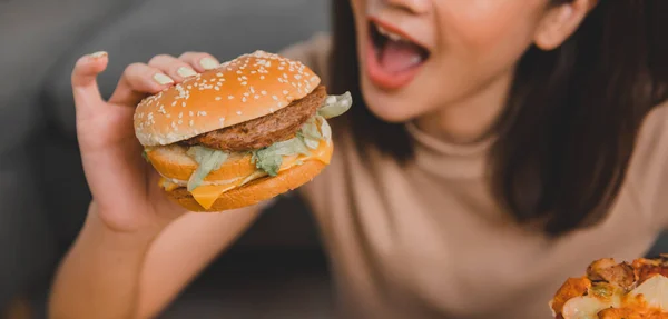 Fast food takeaway back home. Eating burger when takeout and delivery. Asian woman lifestyle in living room. Social distancing and new normal.