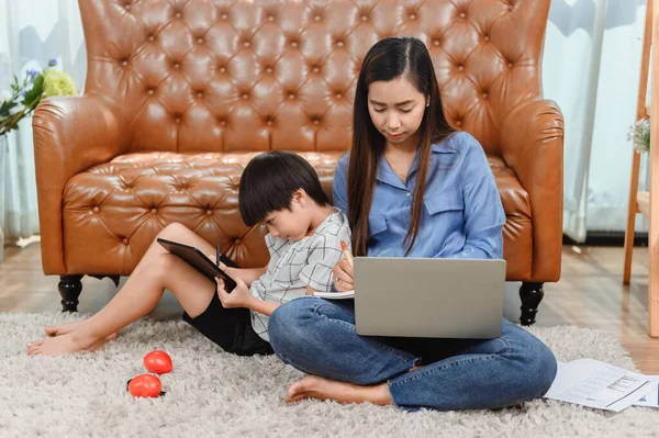 Asian mother work home. Mom together with son. Kid online learning education. New normal lifestyle and family activity.