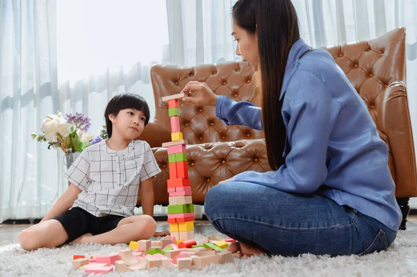 Asian mother work home together with son. Mom and kid play color wooden block. Child creating building toy. Woman lifestyle and family activity.