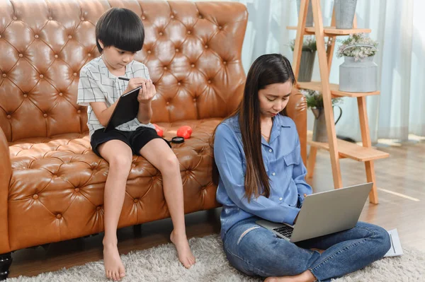 Asian mother work home. Mom together with son. Kid online learning education. New normal lifestyle and family activity.