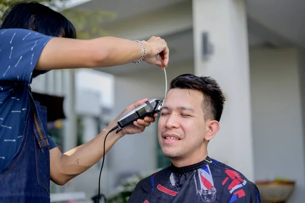 Asian man making haircut and salon business at home. Outdoor barbershop in garden. Social distancing and New normal lifestyle.