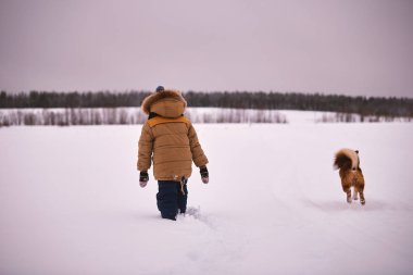 karlı bir alan ile bir köpek kış giysileri içinde küçük çocuk açıktır
