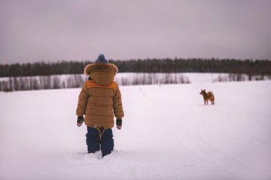 karlı bir alan ile bir köpek kış giysileri içinde küçük çocuk açıktır