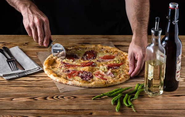 The guy cuts pizza on a wooden table