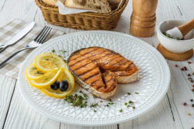 Limonlu ızgara balık ve ahşap beyaz arka planda otlar.