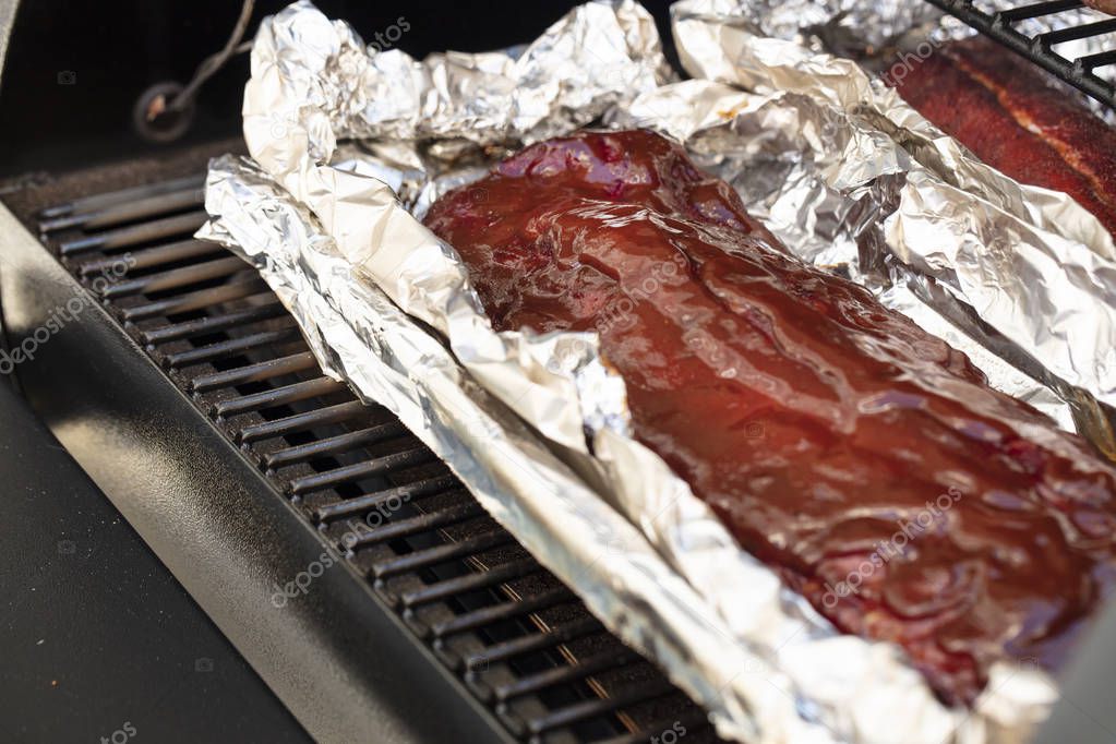 A slab of short ribs  with barbecue sauce on a grill gate and aluminum foil