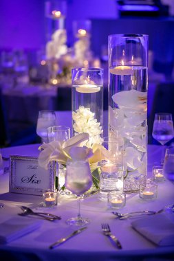 Mavi ışıklı düğün merasimi masaları, yanan cam kaplar ve yüzen mumlarla.