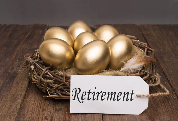 Nest with golden eggs with a tag and a word retirement on a wooden background. The concept of successful retirement — Stock Photo, Image