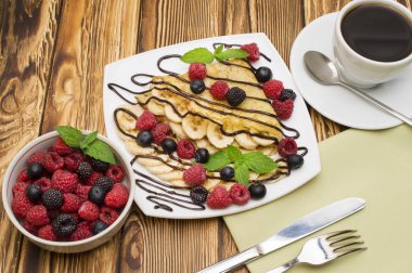 Çikolatalı krema ile servis ev yapımı krep muz, taze yaban mersini, ahududu ahşap zemin, krep