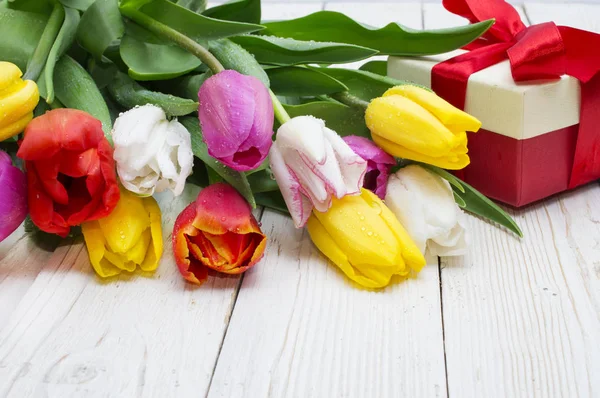 Ramo de tulipanes con un regalo sobre tabla de madera rústica — Foto de Stock