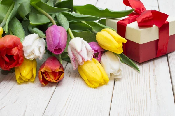 Ramo de tulipanes con un regalo sobre tabla de madera rústica — Foto de Stock