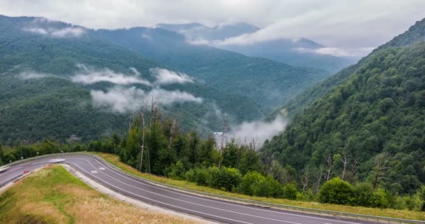 The onset of twilight in the mountains and the appearance of fog on a mountain serpentine, Evening mountain time lapse with the lights of a fast passing vehicle in the fog — Stock Video