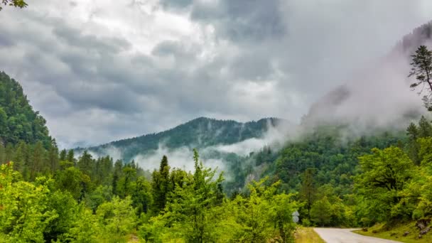 El inicio del crepúsculo en las montañas y la aparición de niebla en una serpentina de montaña, el tiempo de la noche de montaña caducan con las luces de un vehículo de paso rápido en la niebla . — Vídeo de stock