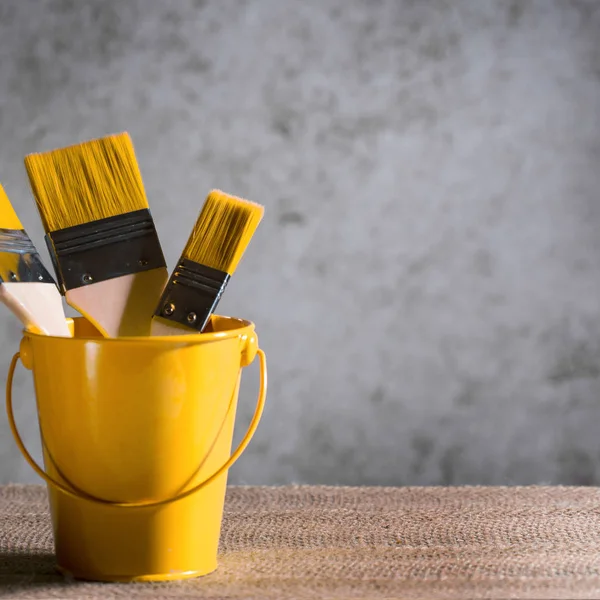 Wide paint brushes in a cute bucket on an artistic blurred background